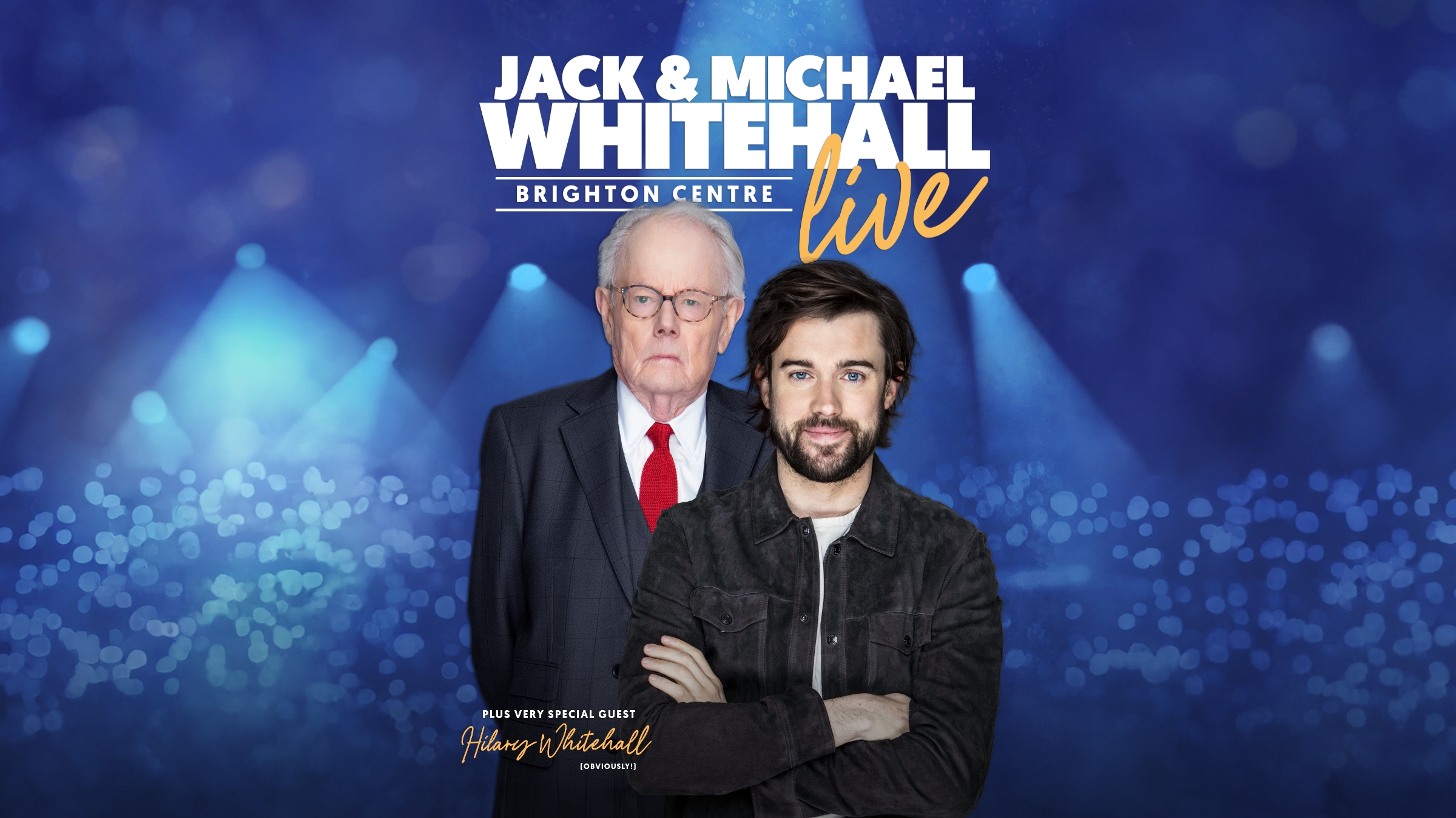 Jack & Michael Whitehall pictured together facing straight to camera. Jack has his arms folded smiling as his Dad looks over Jack's shoulder not smiling