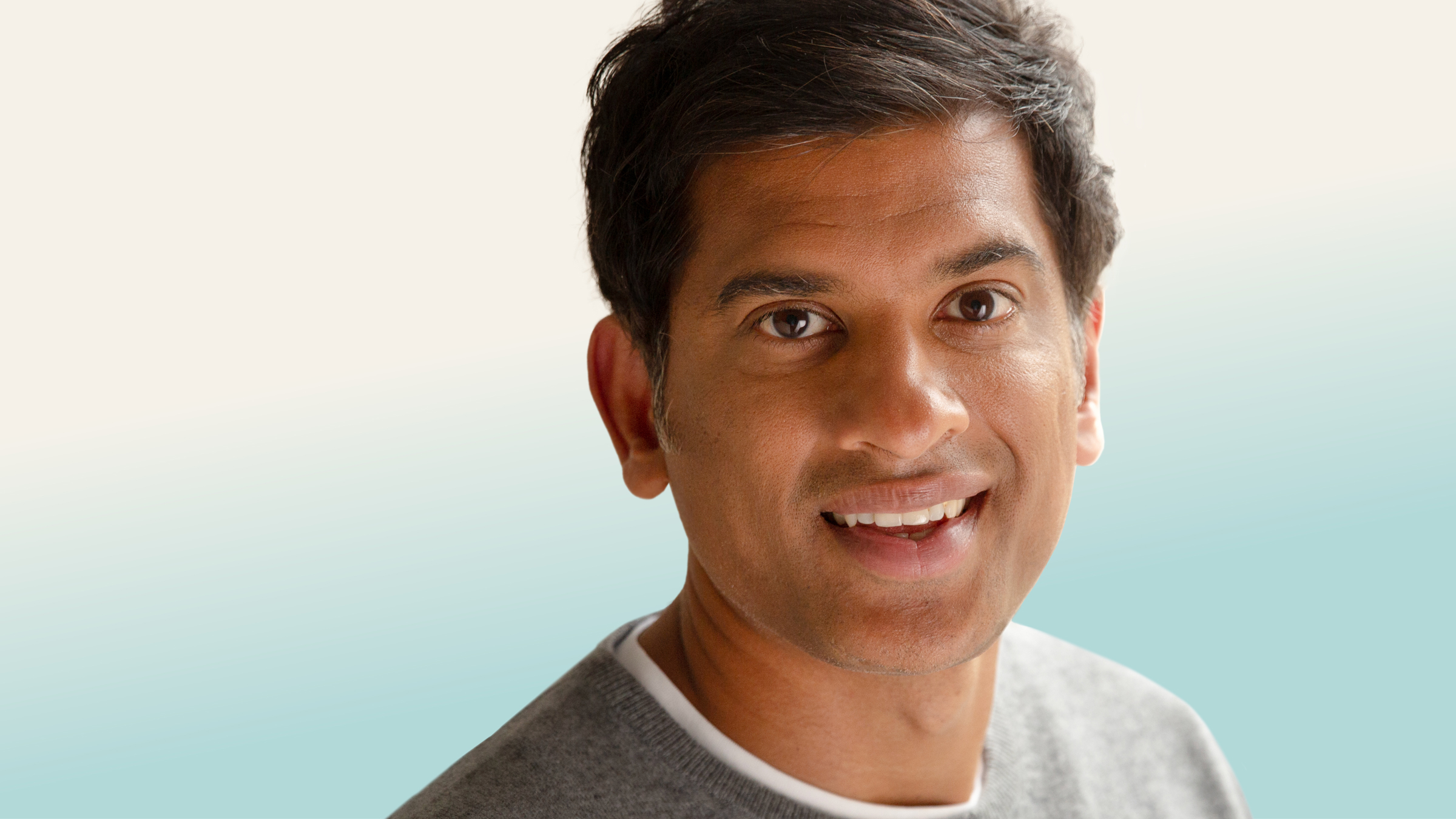 Official tour pic of Dr Rangan Chatterjee. Head and shoulders shot looking and smiling direct to camera, wearing a round neck grey jumper.