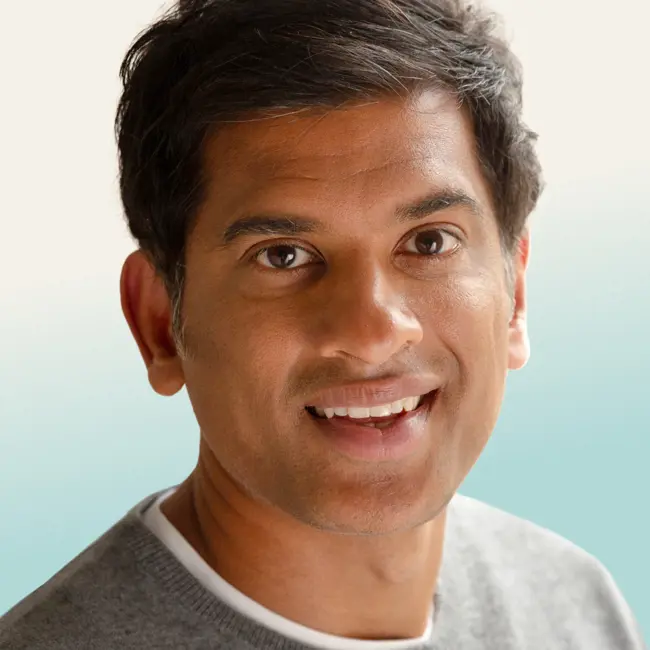 image Official tour pic of Dr Rangan Chatterjee. Head and shoulders shot looking and smiling direct to camera, wearing a round neck grey jumper.