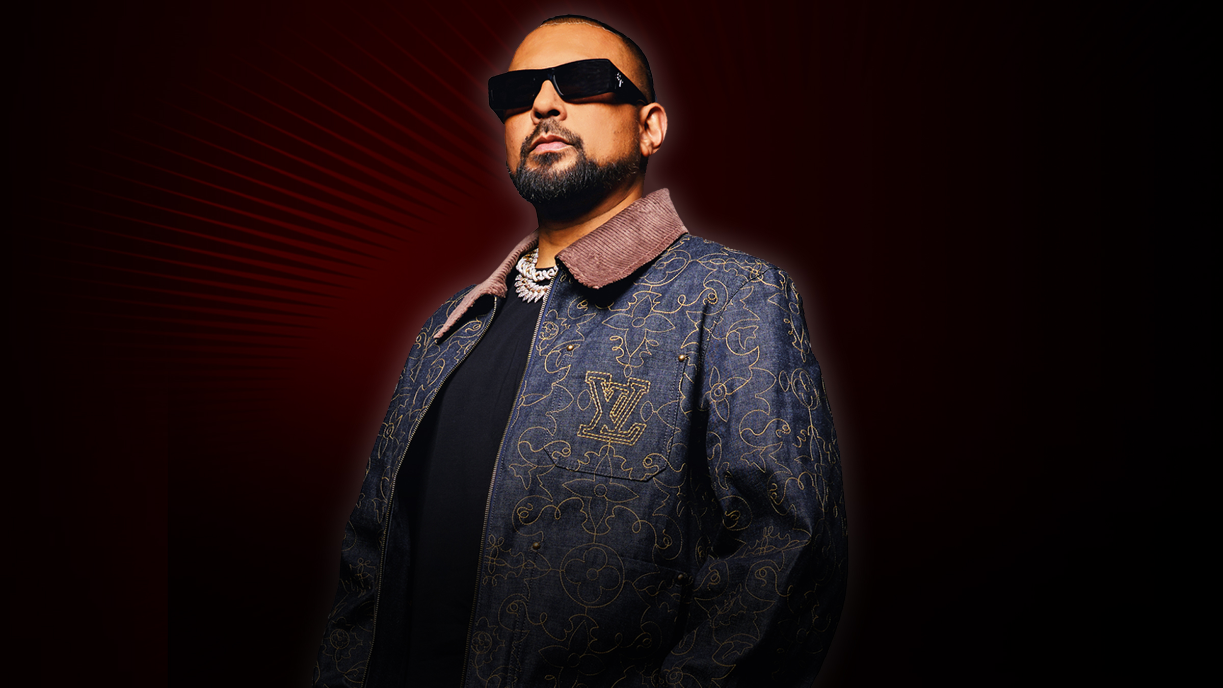 Sean Paul stands in dark jackets and T shirt wearing dark glasses. He has red beams of light radiating from behind him.