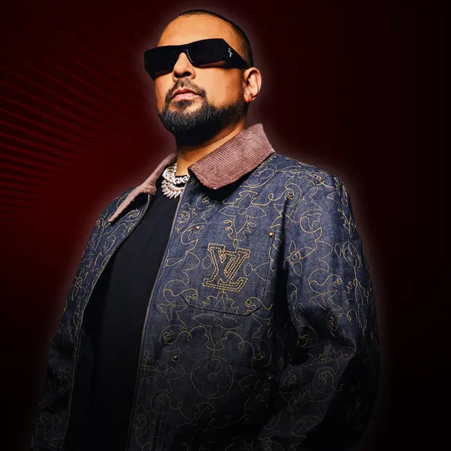 image Sean Paul stands in dark jackets and T shirt wearing dark glasses. He has red beams of light radiating from behind him.