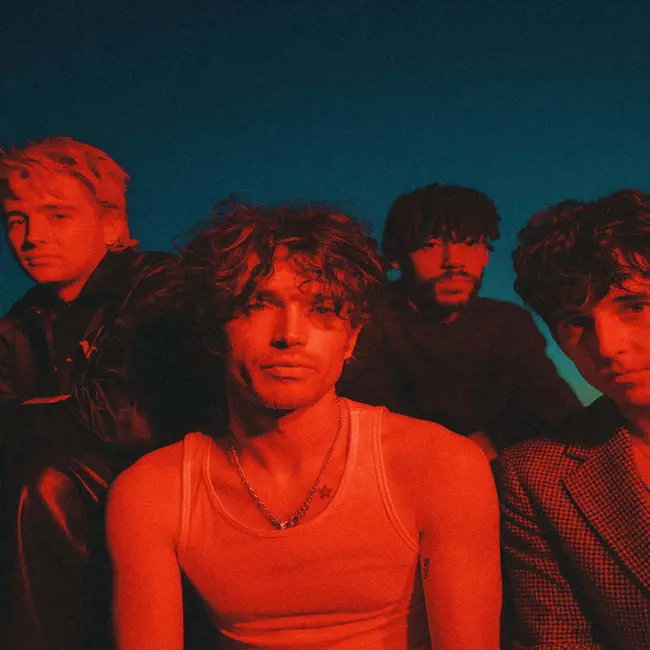 image INHALER official tour pic. Four band members are sat together in a red light. All look to camera. Backdrop of a night sky.